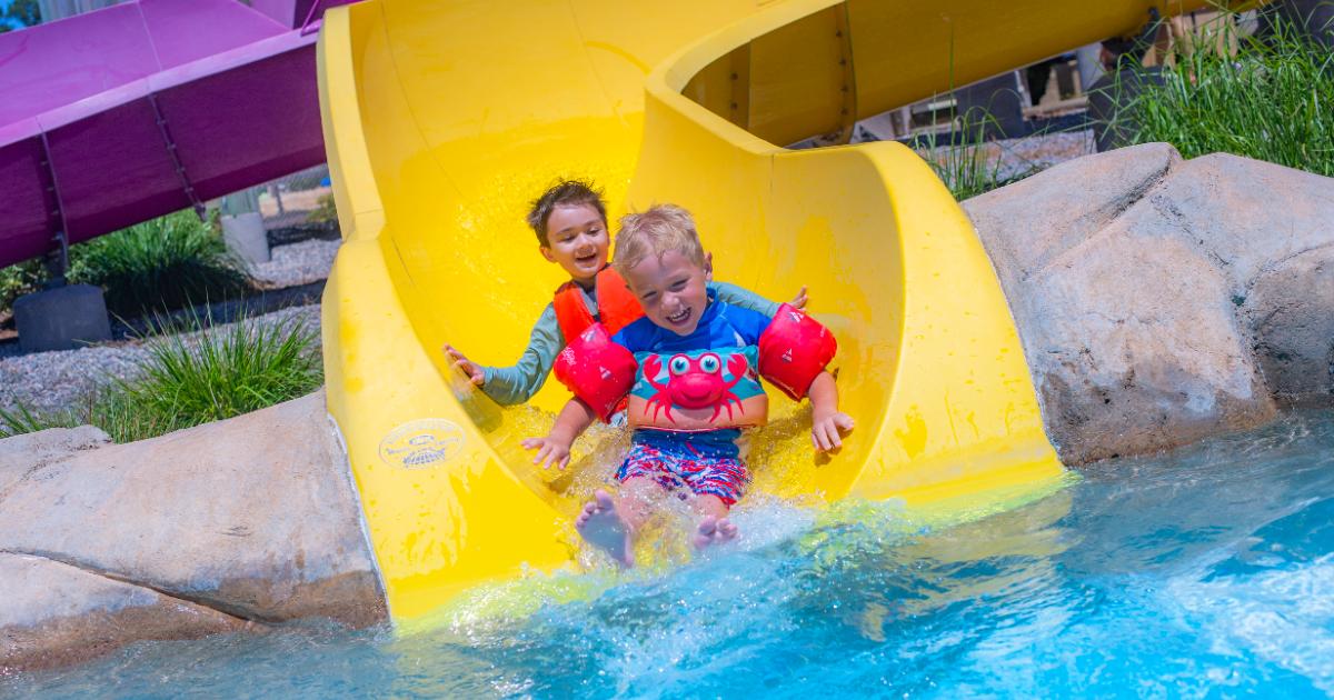 Two boys sliding down yellow slide