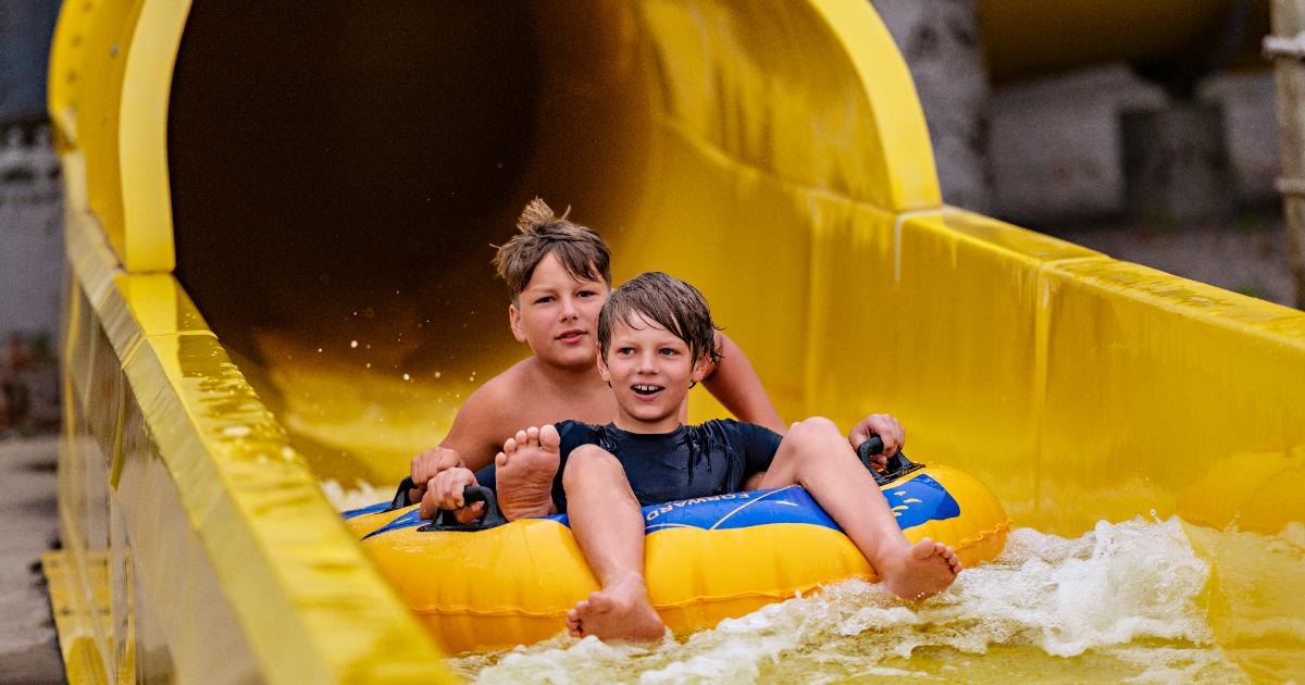 Two boys sliding down yellow slide